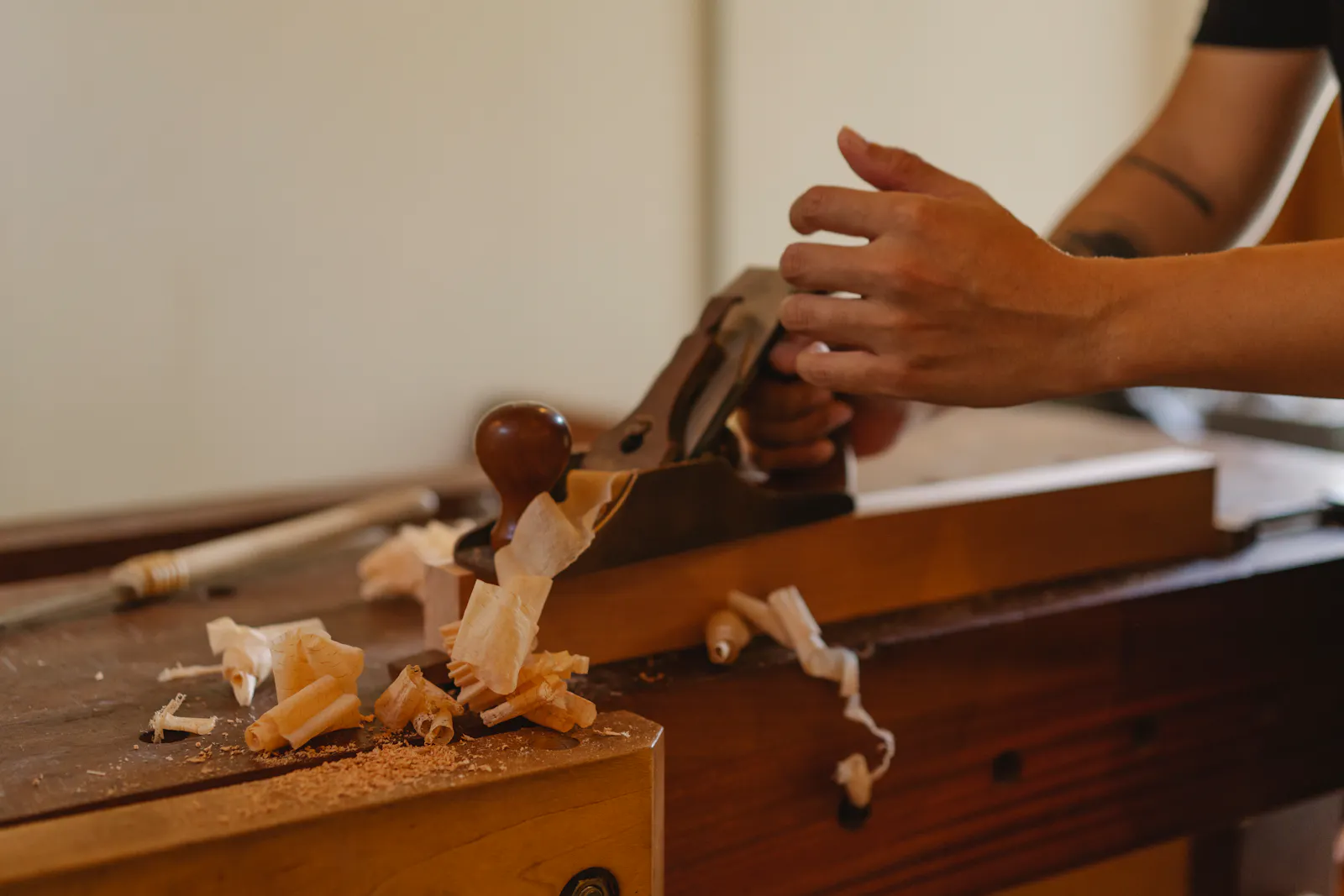 Mains de l'artisan rabotant une planche, copeaux de bois